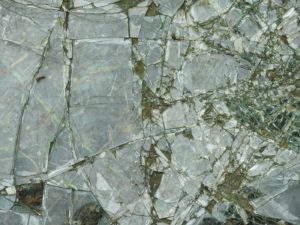 alt text: image is a color photograph of shattered glass; title card for the essay "Like Water Flowing" by April Bradley