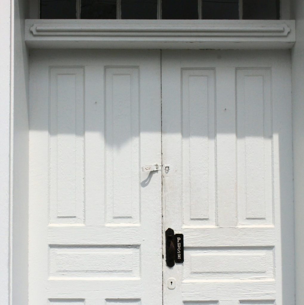 alt text: image is a color photograph of white church doors; title card for Jane Marcellus's flash nonfiction piece "Kept"