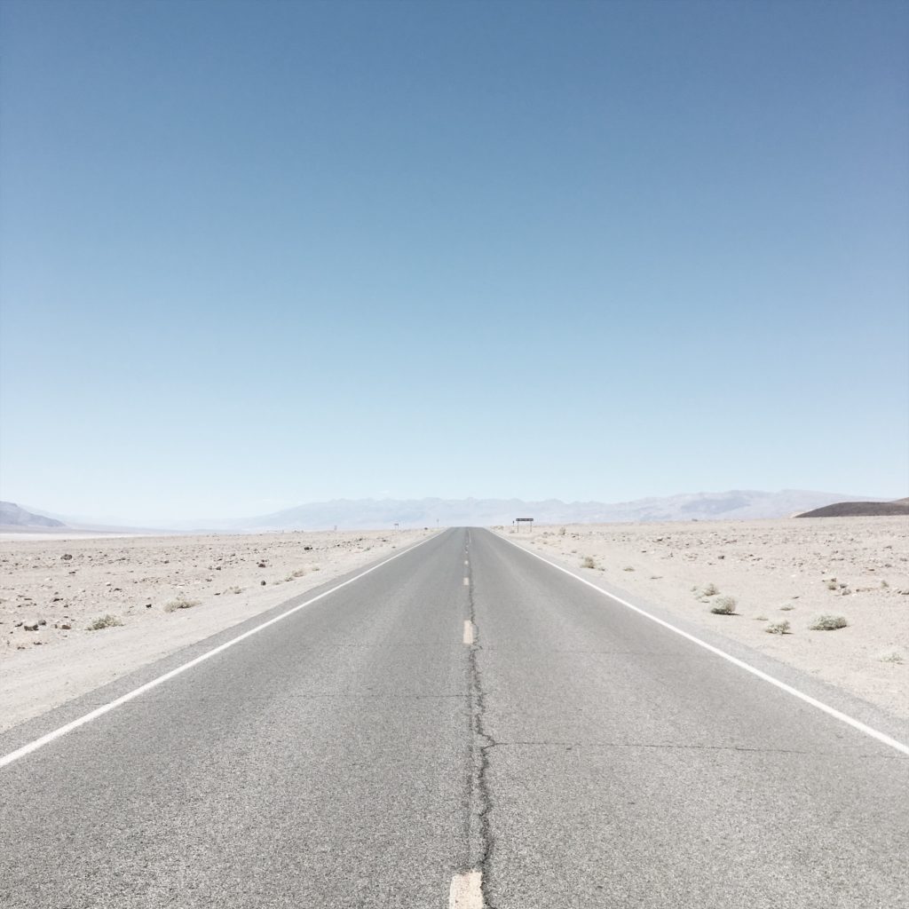 alt text: image is a color photograph of a desert road; title card for the flash fiction piece "De Nuevo" by A.J. Rodriguez