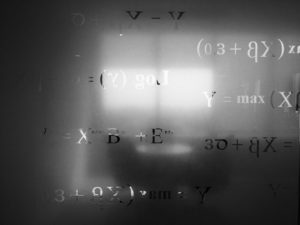 alt text: image is a black-and-white photograph of a board with mathematical equations; title card for Beth Gistrap's creative nonfiction piece "The Pythagorean Theorem: Three Micros"