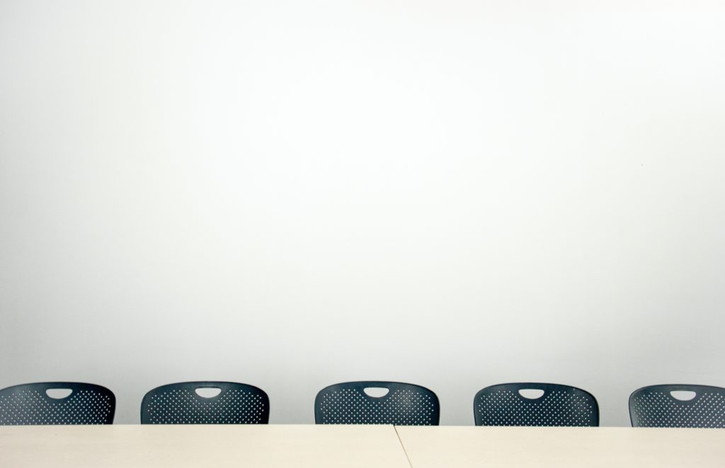 alt text: image is a color photograph of classroom chairs pushed up against a desk; title card for Amy Evan's creative nonfiction piece "The Stoics"