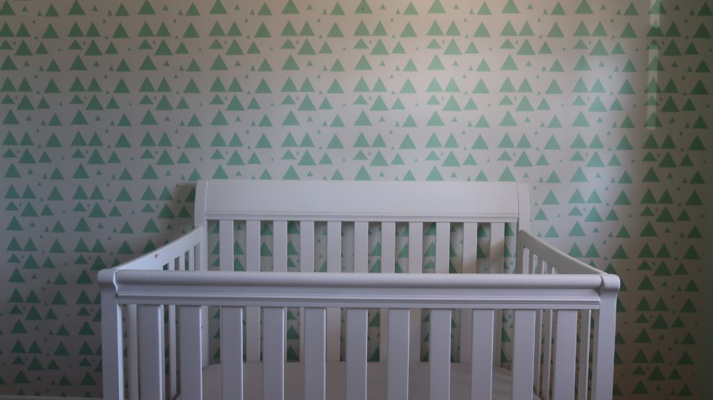alt text: image is a color photograph of a baby's crib; title card for the flash fiction pieces "Genetically Predetermined Chemical Imbalances" by Eliot Li