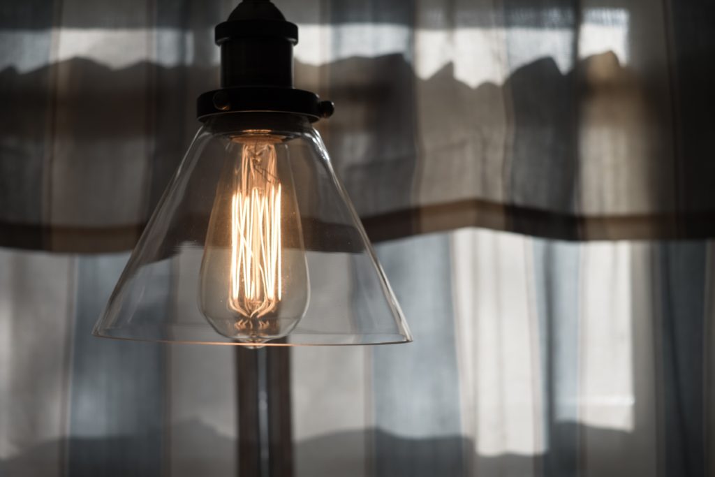 alt text: image is a color photograph of a clear light bulb; title card for the flash essay "Our Therapists Will Tell Us to Call It an Inpatient Facility" by Max Hunt