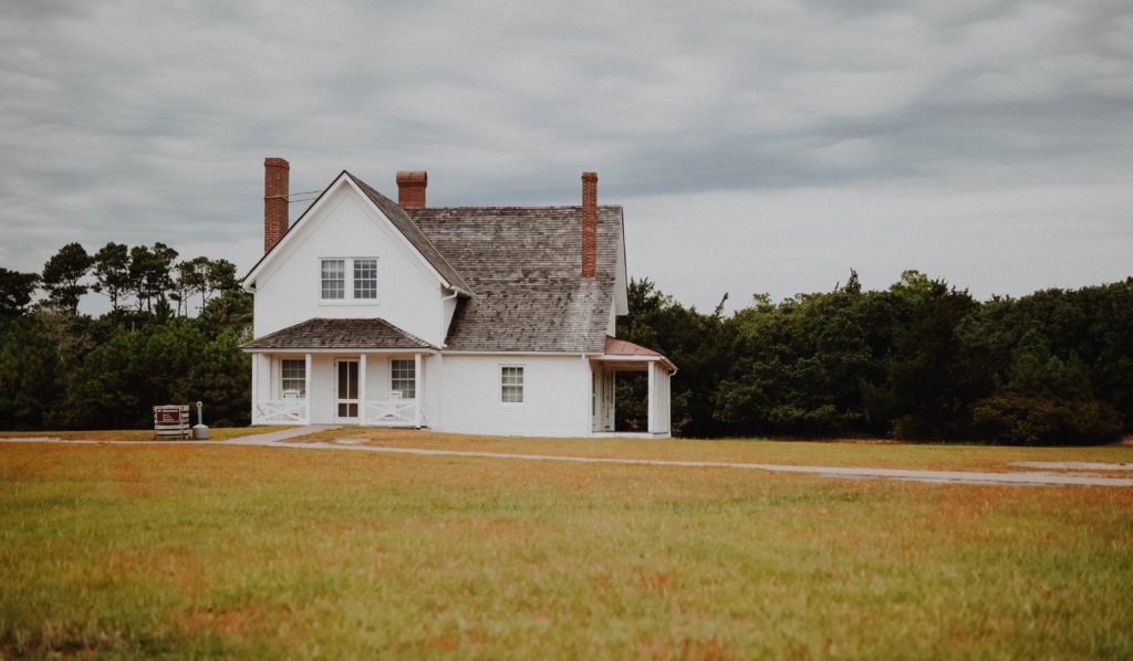 alt text: image is a color photograph of a white house on a large lawn; title card for new flash fiction "The Final Girl as a Middle-Aged Woman" by Amber Sparks