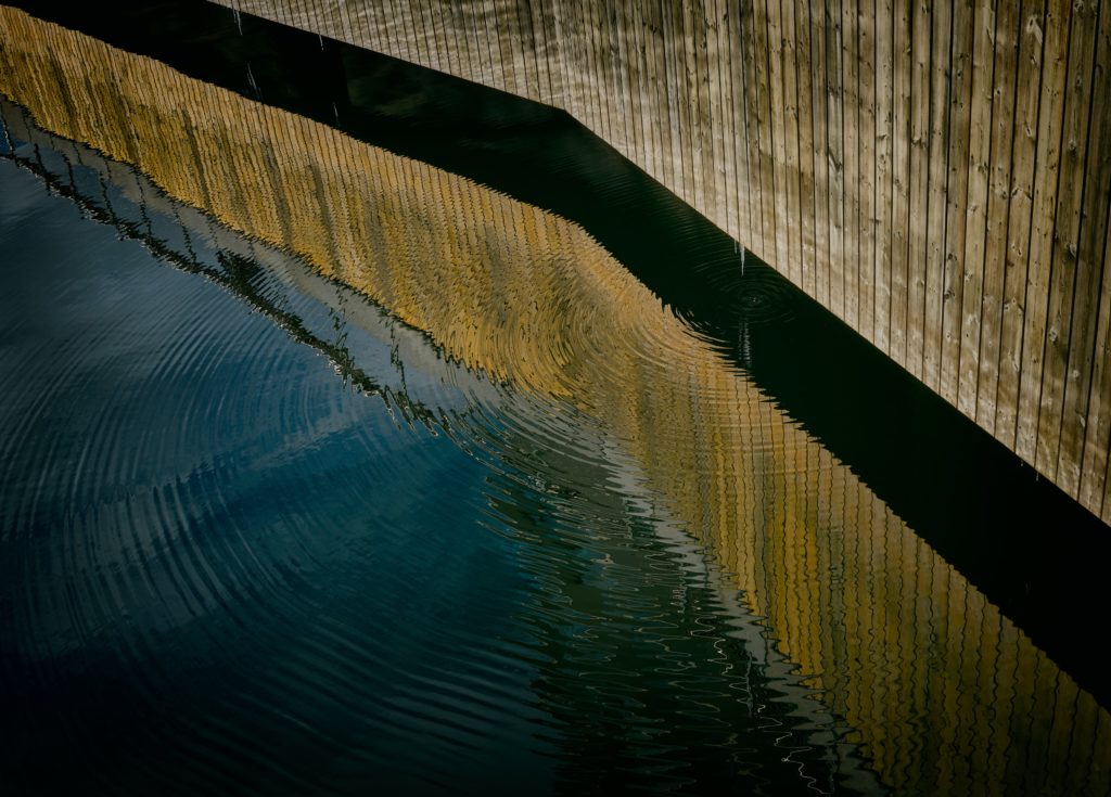 Image is a photograph of a wooden board wall dripping water into a pool, causing ripples; title card for the new critical essay "Crafting Endings in Short Fiction" by Jennifer Murvin.