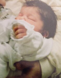 Image is a photograph of a newborn, Rowan's youngest, with lots of dark hair.