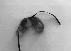 Image is a photograph of another lock of hair, tied with black ribbon.