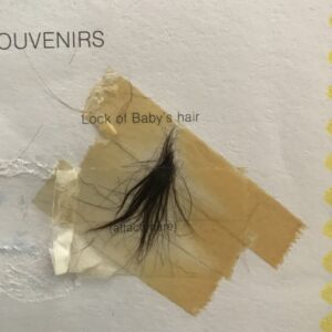 Image is a photograph of a lock of baby hair taped into a keepsake album.