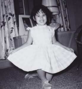 Image shows a young girl, the author, in a white dress with a full skirt.