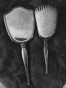 Image is a photograph of a silver grooming set, a hairbrush and mirror.
