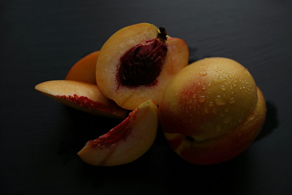 Image is a color photograph of sliced nectarines; title card for the 2024 Flash Prose Prize Editors’ Choice Selection, “My Mother the Nectarine,” by Megan Haeuser.